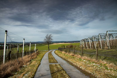 Road passing through field against sky