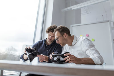 Engineers examining virtual reality simulators at table in office