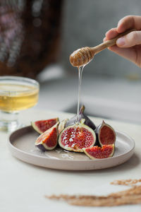 Honey drips from honey wooden stick to pieces of fresh ripe figs on stylish ceramic plate