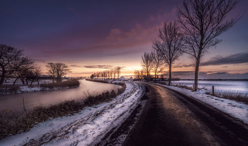 Snow covered road against sky during sunset