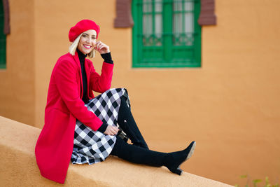 Side view of young woman sitting against wall