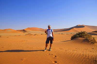 Woman standing on sand dune in desert against clear sky