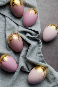 Easter eggs are painted with gold and violet paint on a gray linen background. 