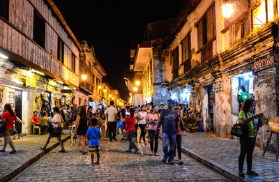 People walking on illuminated street amidst buildings at night