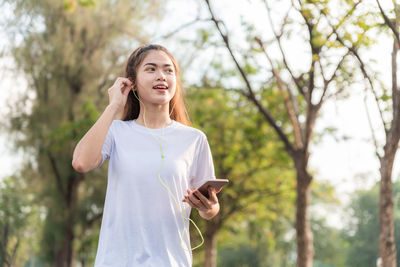 Young woman using phone while standing on tree