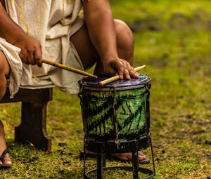 Low section of man playing drum while sitting on land