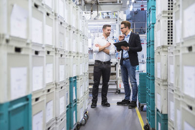 Two men with tablet talking at boxes in factory shop floor