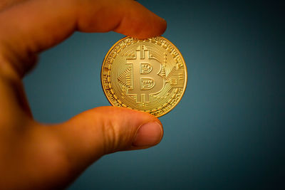 Close-up of hand holding coin against gray background