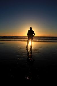 Silhouette man standing on beach against clear sky during sunset