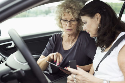 Senior female friends using digital tablet in car