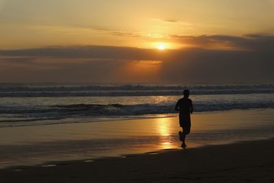 Silhouette of jogger on beach against sky during sunset