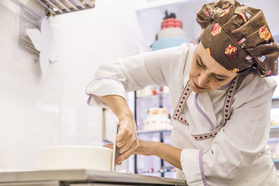 Low angle view of female baker making cake with smoother on kitchen counter in laboratory