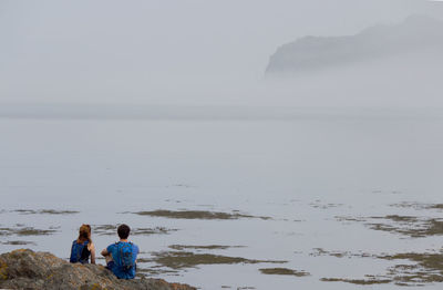 Rear view of people standing at beach against sky