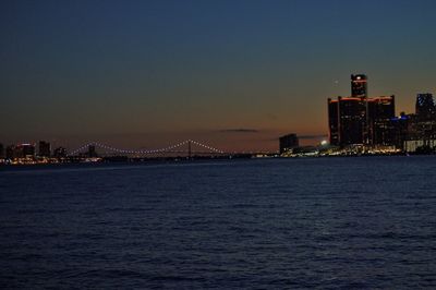 Sea by illuminated city against sky at night