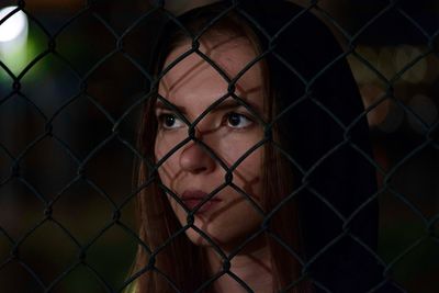 Portrait of young woman seen through chainlink fence
