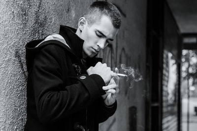 Young man smoking while standing against wall