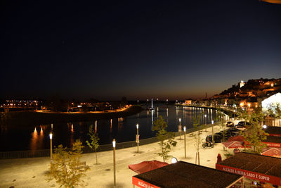 Illuminated cityscape by sea against clear sky at night