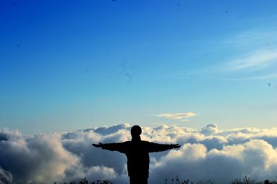 Silhouette man with arms outstretched standing against sky