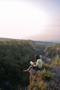 Side view of man sitting on landscape against clear sky