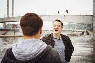 Smiling man talking with friend against bridge in city