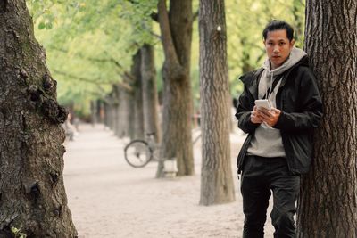 Full length of young man holding tree trunk