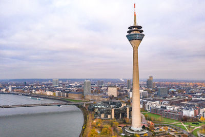 Communications tower in city against cloudy sky