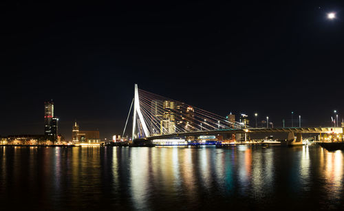 Illuminated erasmus bridge over sea against sky at night in city