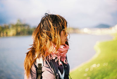 Side view of hooded woman standing at lakeshore against sky