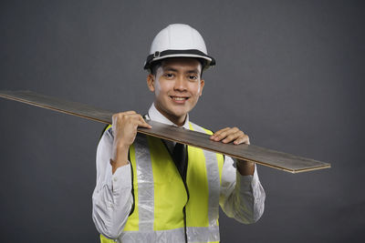 Portrait of young man holding hat against gray background