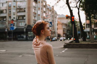 Young redheaded woman holding hair while standing in city street
