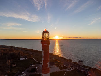 Lighthouse by sea against sky during sunset