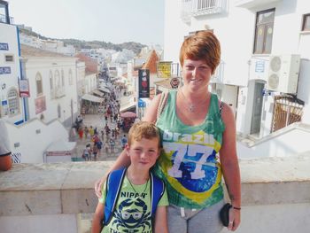 Portrait of smiling woman with boy standing against buildings