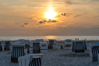 Hooded chairs on beach against sky during sunset