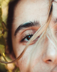 Closeup of crop young female with brown eyes looking at camera against green leaves in nature