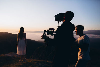 People photographing woman against sky during sunset