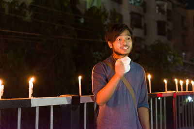 Young man standing against illuminated railing at night