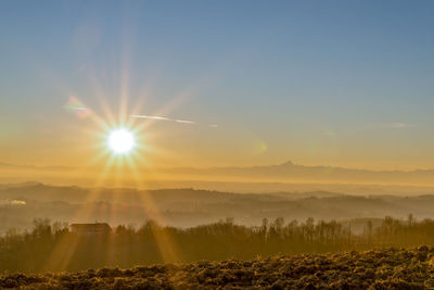 Sunlight streaming through trees on landscape against sky during sunset