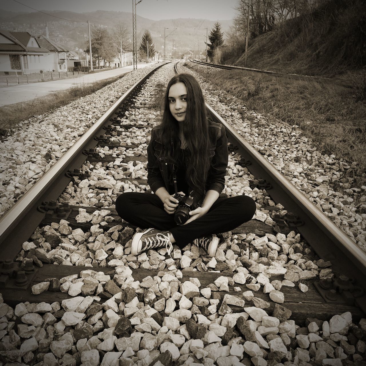 railroad track, track, rail transportation, one person, sitting, young adult, young women, real people, solid, full length, lifestyles, casual clothing, front view, nature, leisure activity, stone - object, portrait, day, rock, gravel, diminishing perspective, pebble, outdoors, teenager, hairstyle, beautiful woman, contemplation