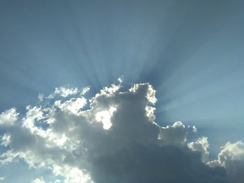 Low angle view of sunlight streaming through clouds