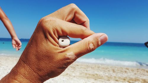 Close-up of woman hand holding sand at beach against clear blue sky