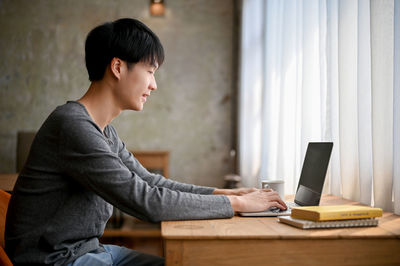 Side view of young man using laptop at office