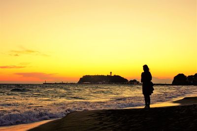 Silhouette woman standing at beach against sky during sunset