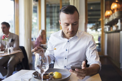 Businessman eating lunch while using mobile phone at restaurant