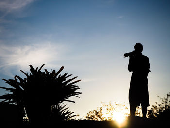 Silhouette man photographing against sky during sunset