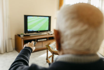 Back view of senior man watching tv at home