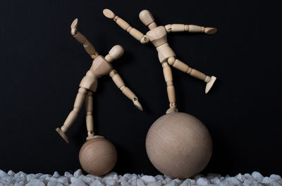 Close-up of wooden figurines balancing on balls against black background