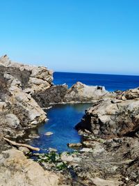 Rocks by sea against clear blue sky