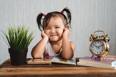 Portrait of cute baby girl with hands on chin resting on table at home