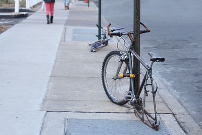 Broken bicycle by pole on footpath