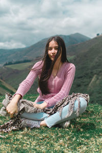 Beautiful young woman sitting on mountain against sky